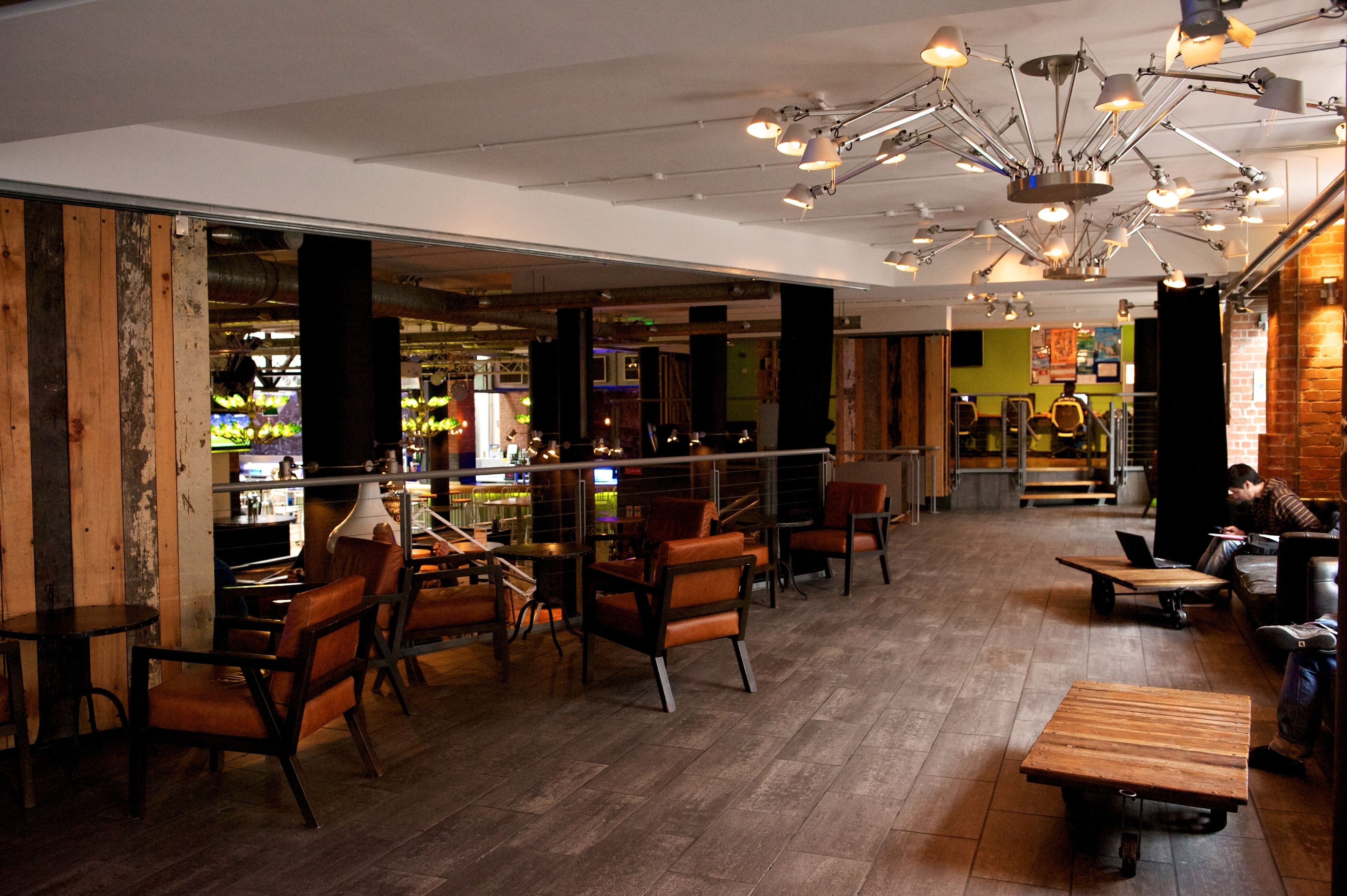 Een ruime binnenzone met houten vloeren, diverse zithoeken met stoelen en tafels, en een bar met krukken.