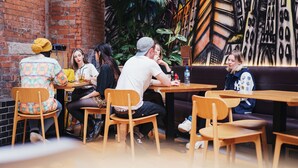 Een café met houten tafels en stoelen, een bakstenen muur en een muurschildering op de achtergrond.