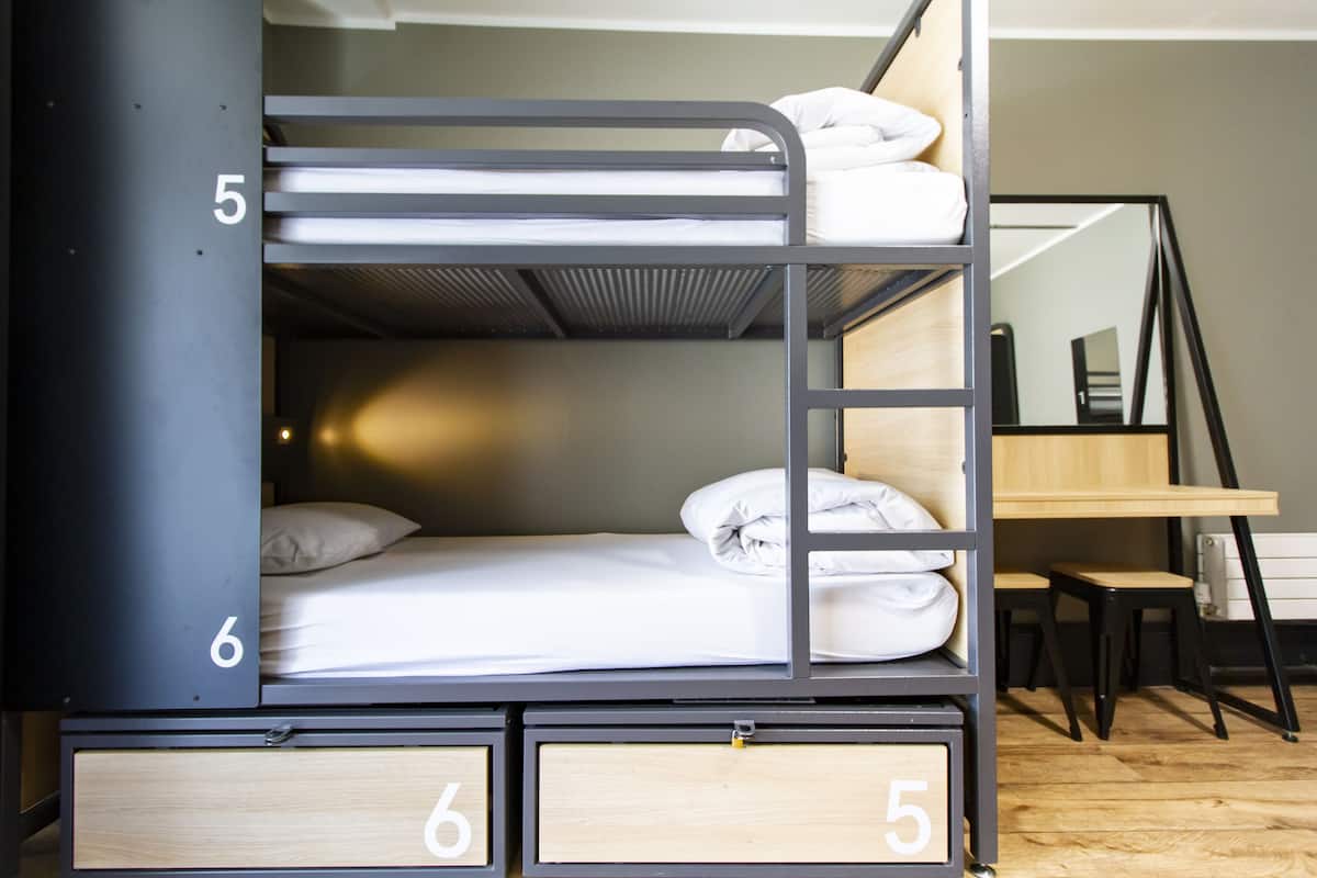 A bunk bed with two levels, each marked with a number. There is a desk and chair to the right, and a mirror on the wall.
