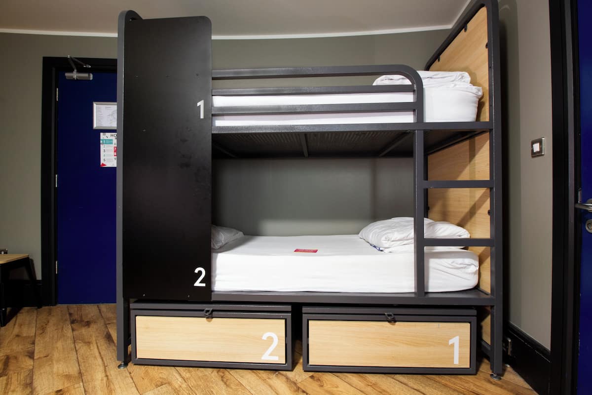 A bunk bed with two drawers, a wooden floor, and a blue door in the background.