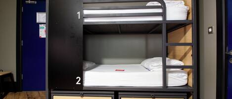 A bunk bed with two drawers, a wooden floor, and a blue door in the background.