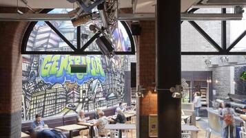 Un café dont un mur est décoré d’une fresque représentant un paysage urbain, avec des tables et des chaises disposées pour accueillir les clients.