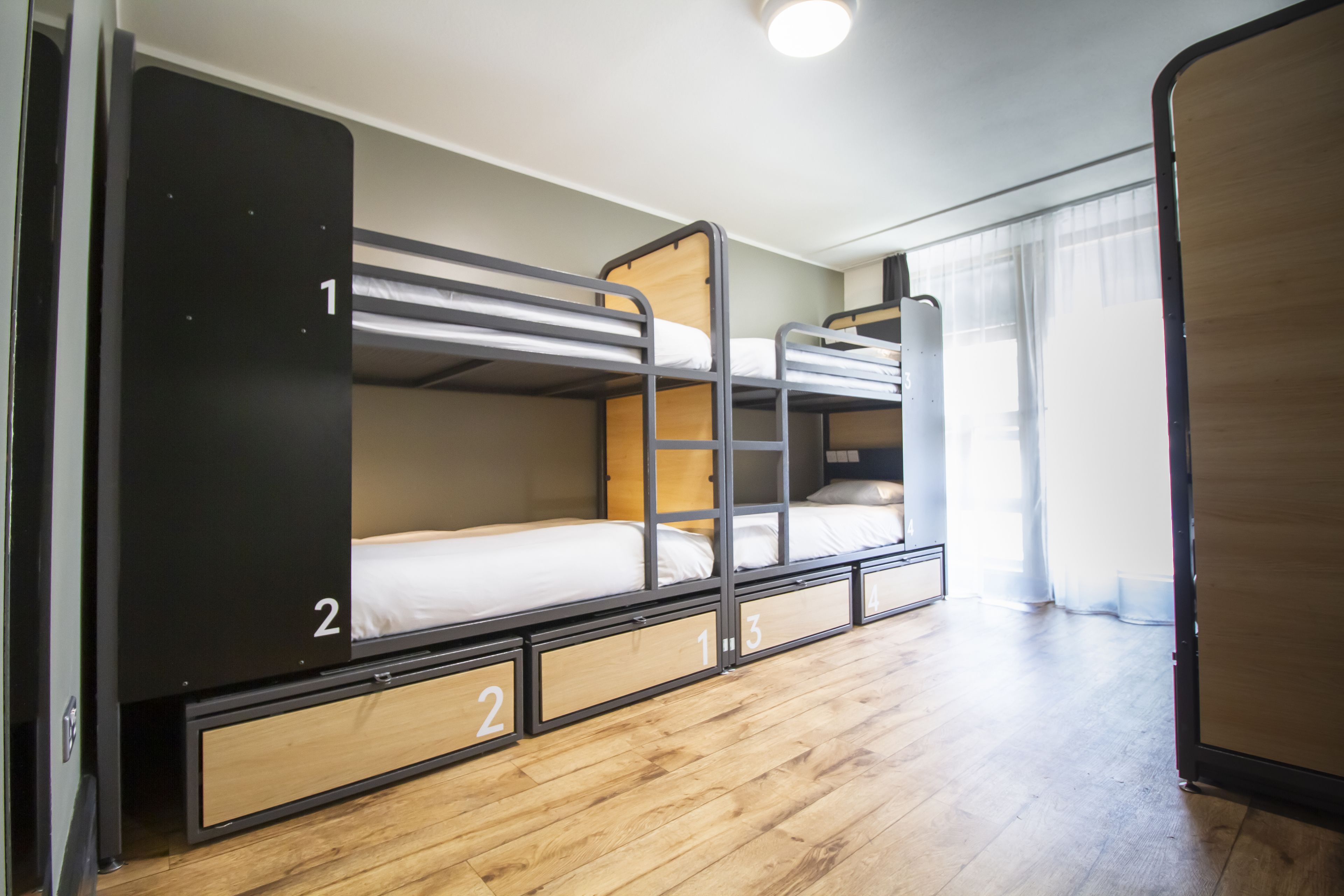 A bunk bed room with wooden flooring and a window with sheer curtains.