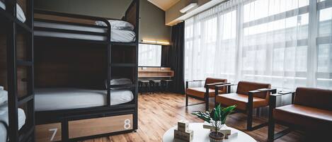 Una habitación con literas, una mesa redonda con una planta y sillones de cuero.