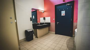 Un baño con un lavamanos negro, un cubo de basura, un espejo y una puerta con un letrero.