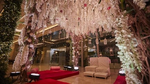 Un décor intérieur luxueux, avec un tapis rouge, des sièges confortables et des décorations florales suspendues.