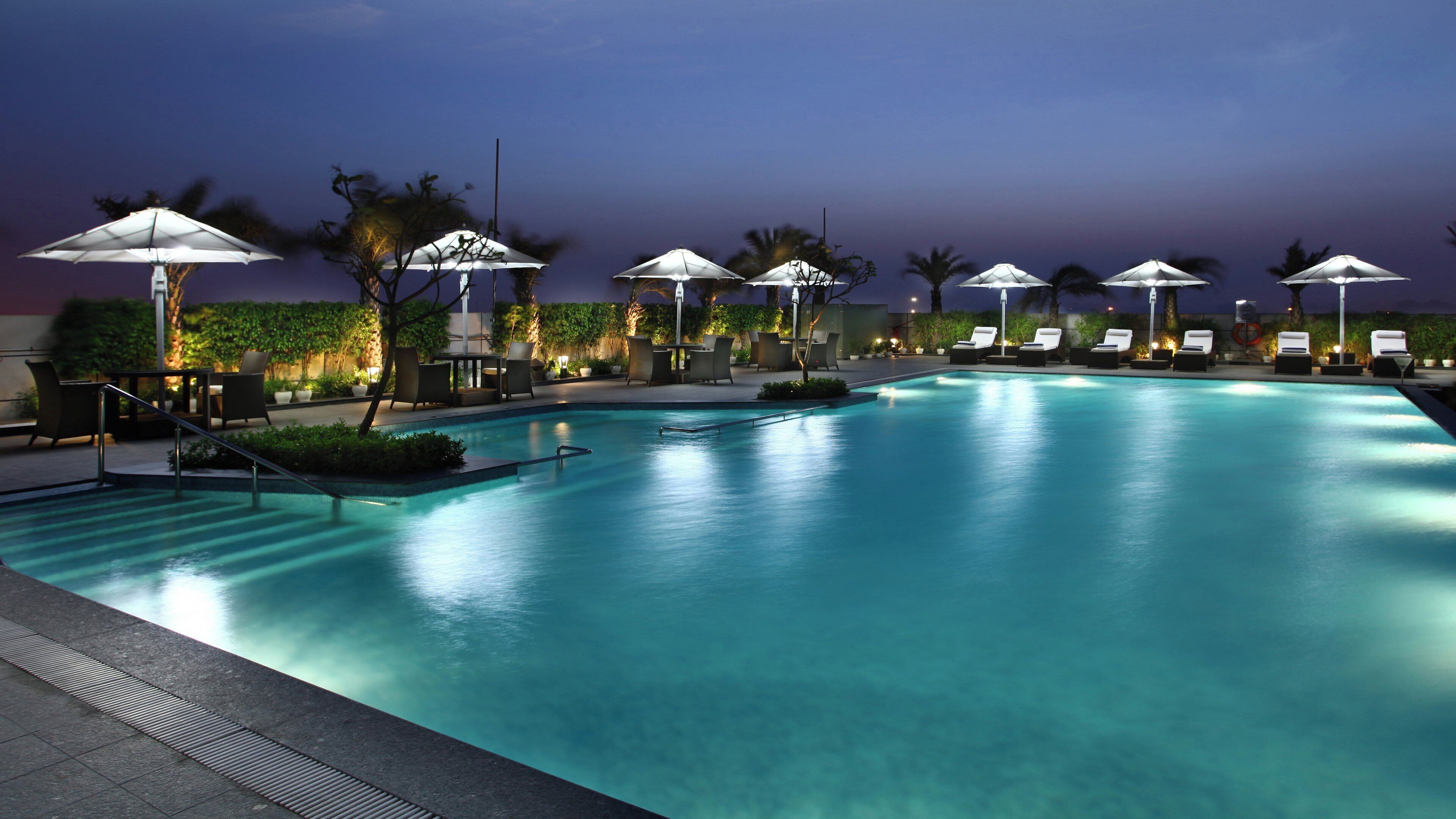A swimming pool with lounge chairs and umbrellas, surrounded by greenery.