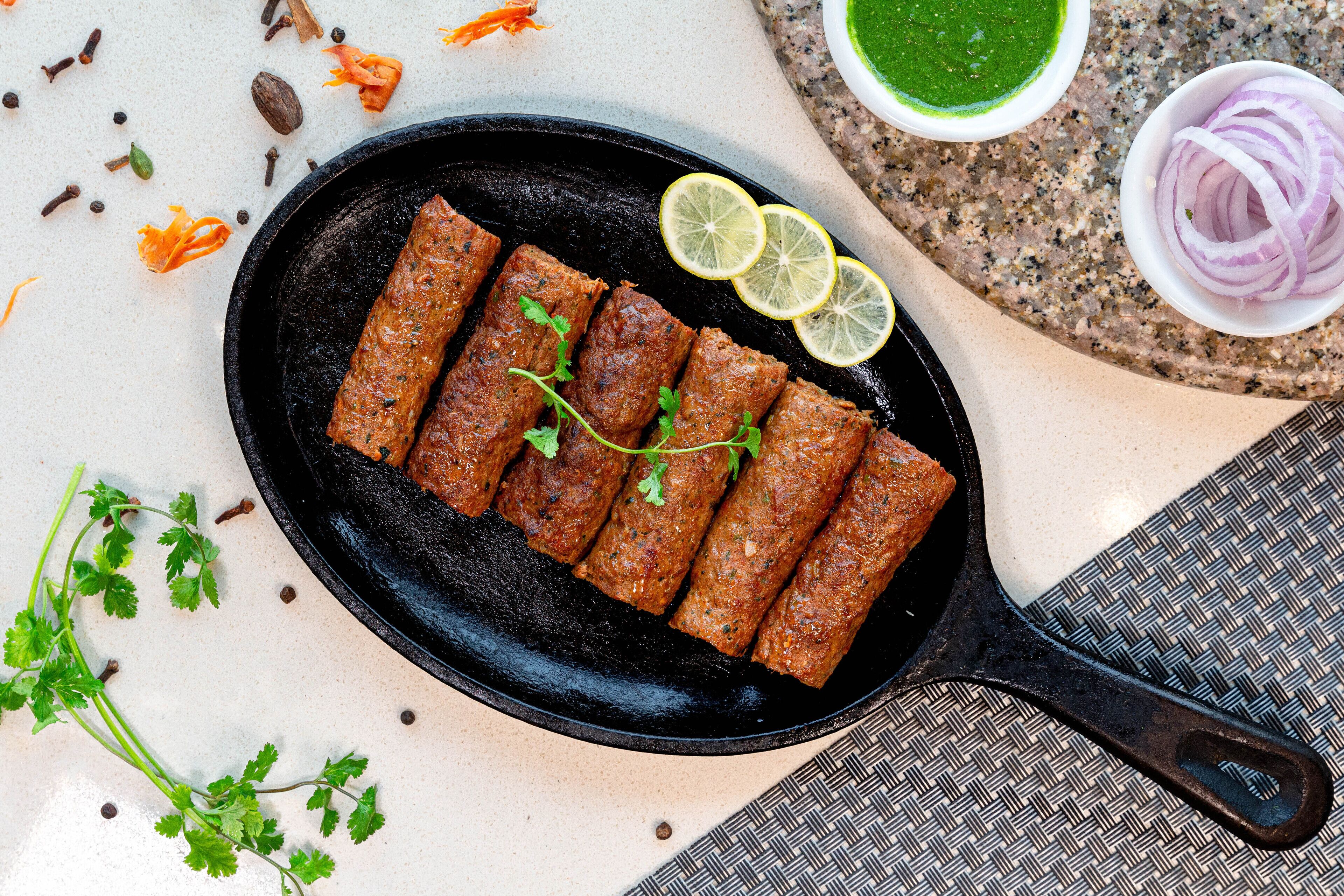 Una sartén con kebabs, rodajas de limón y hierbas sobre una mesa.