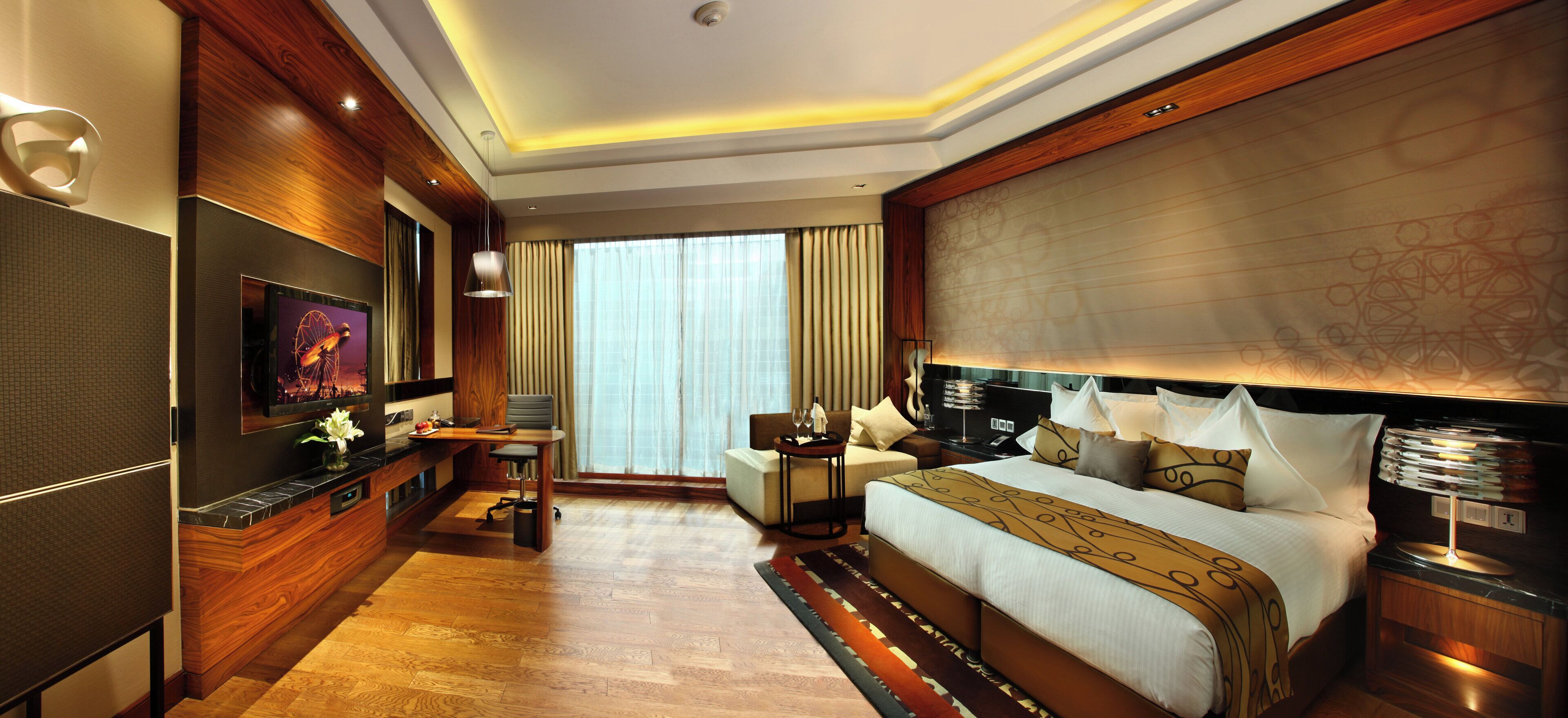 A modern hotel room with a large bed, a desk, a TV, and a view of the city.