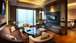 Une chambre d’hôtel moderne équipée d’une grande télévision, de fauteuils confortables, d’un bureau et d’un lit.