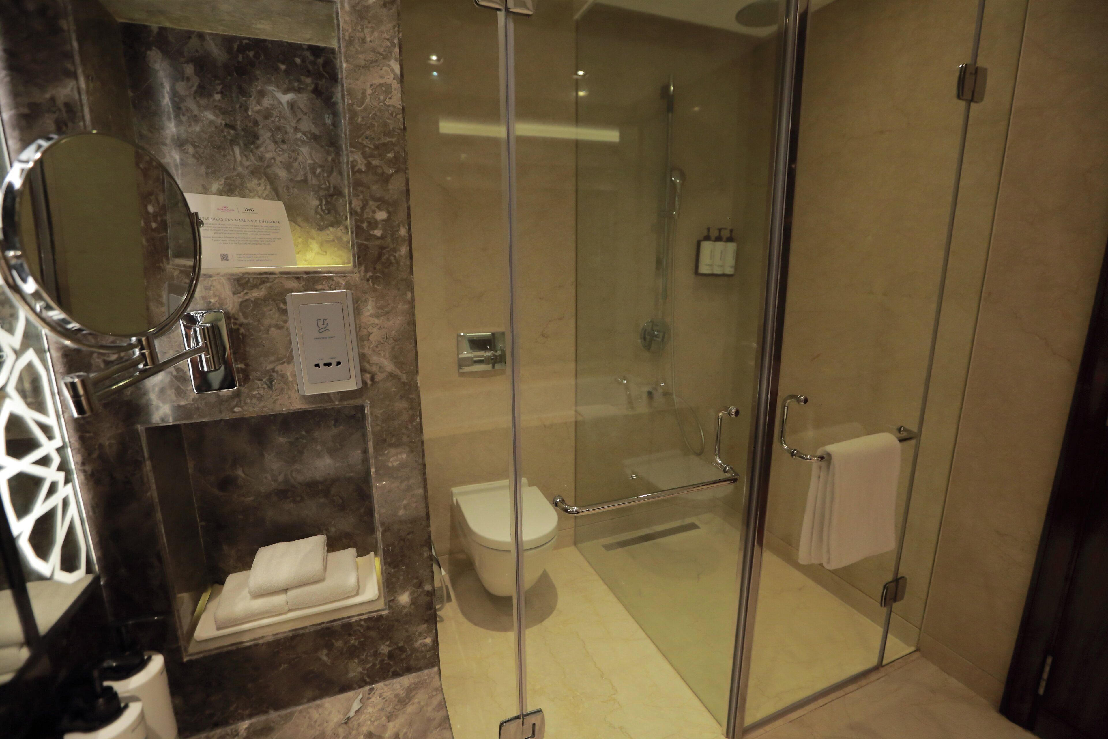 A modern bathroom with a glass-enclosed shower, a toilet, and a vanity with a mirror and towel rack.