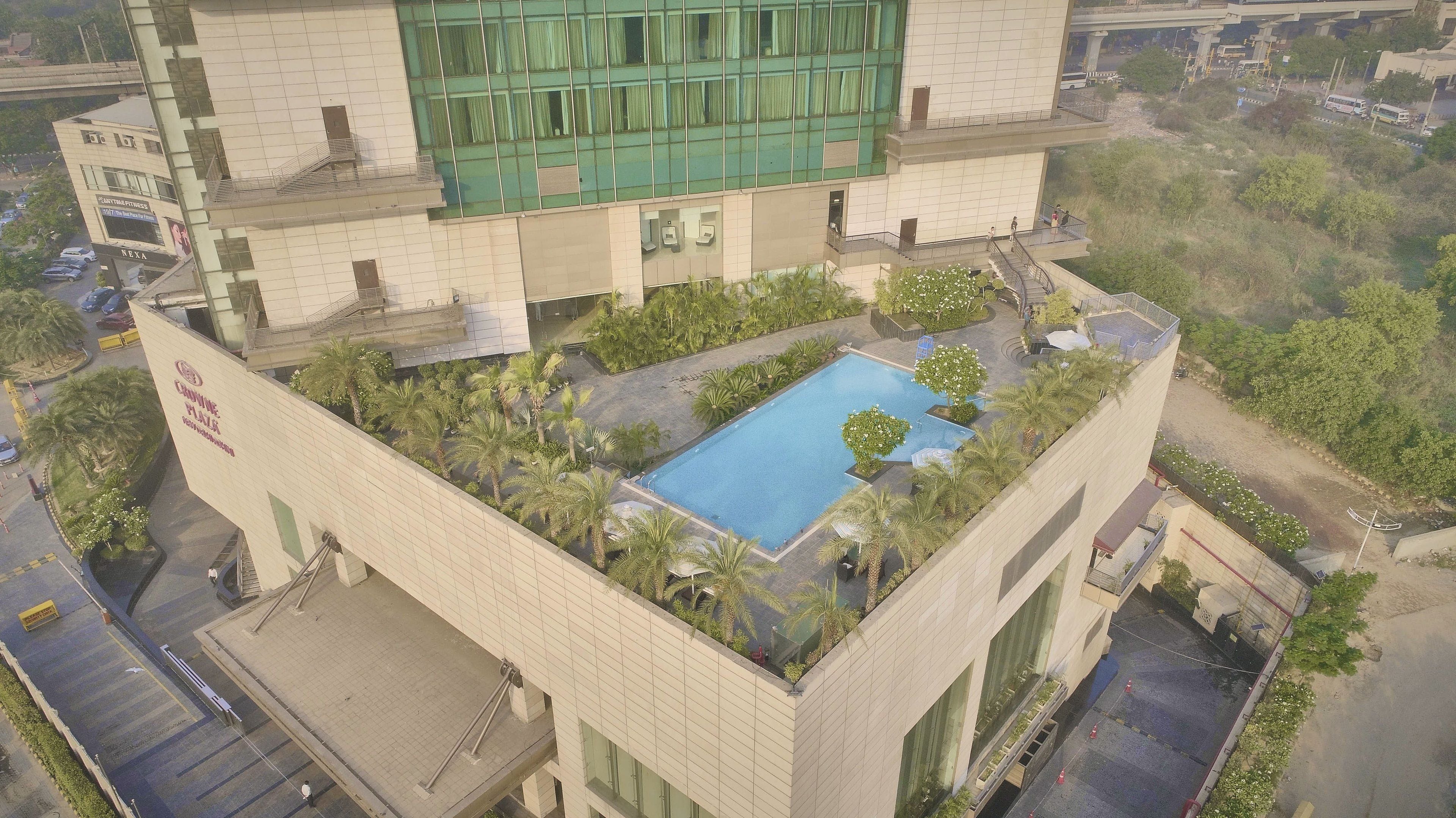 A hotel with a rooftop pool surrounded by greenery, a fitness center, and a parking area.