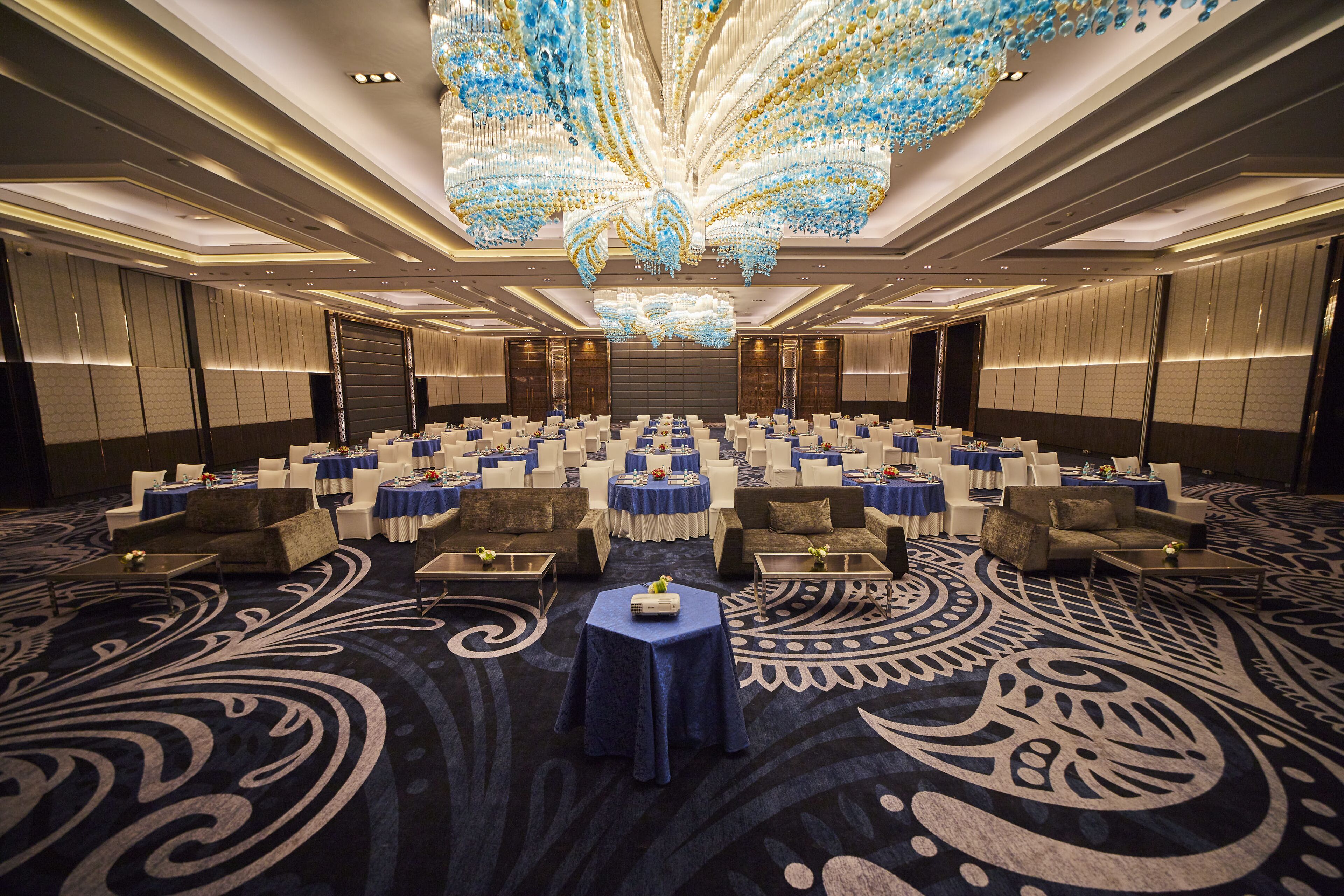 A spacious conference room with rows of tables and chairs, a large chandelier, and a patterned carpet.