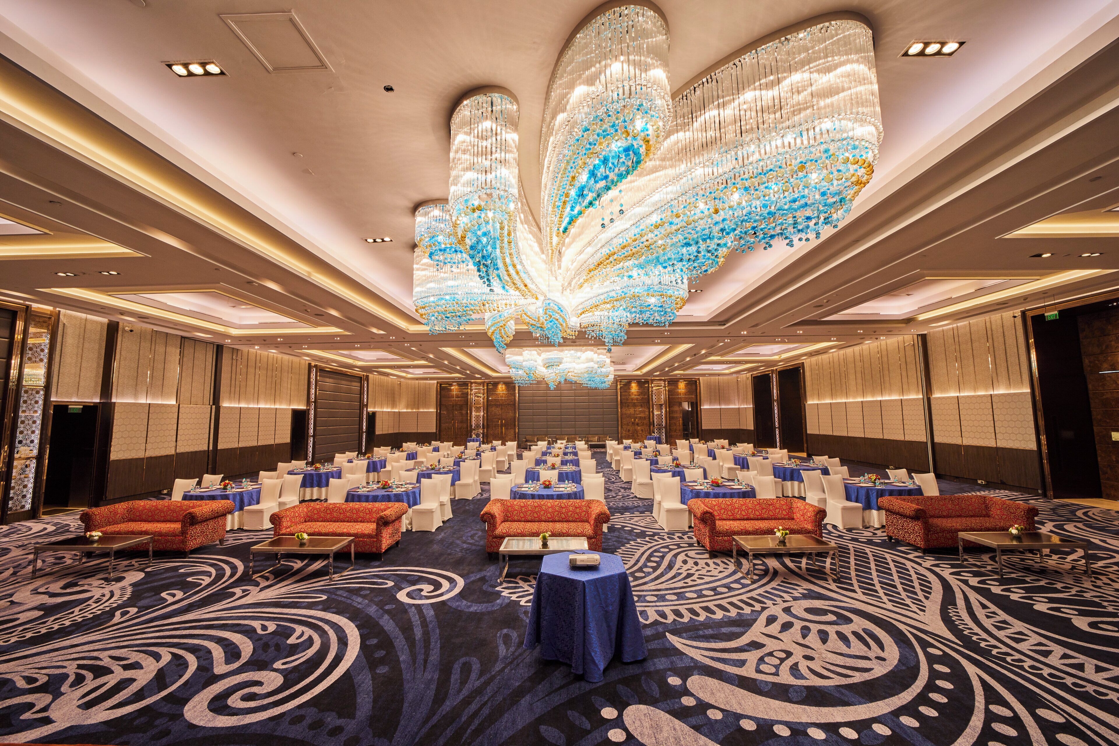 A spacious conference room with rows of tables and chairs, a large decorative chandelier, and a patterned carpet.
