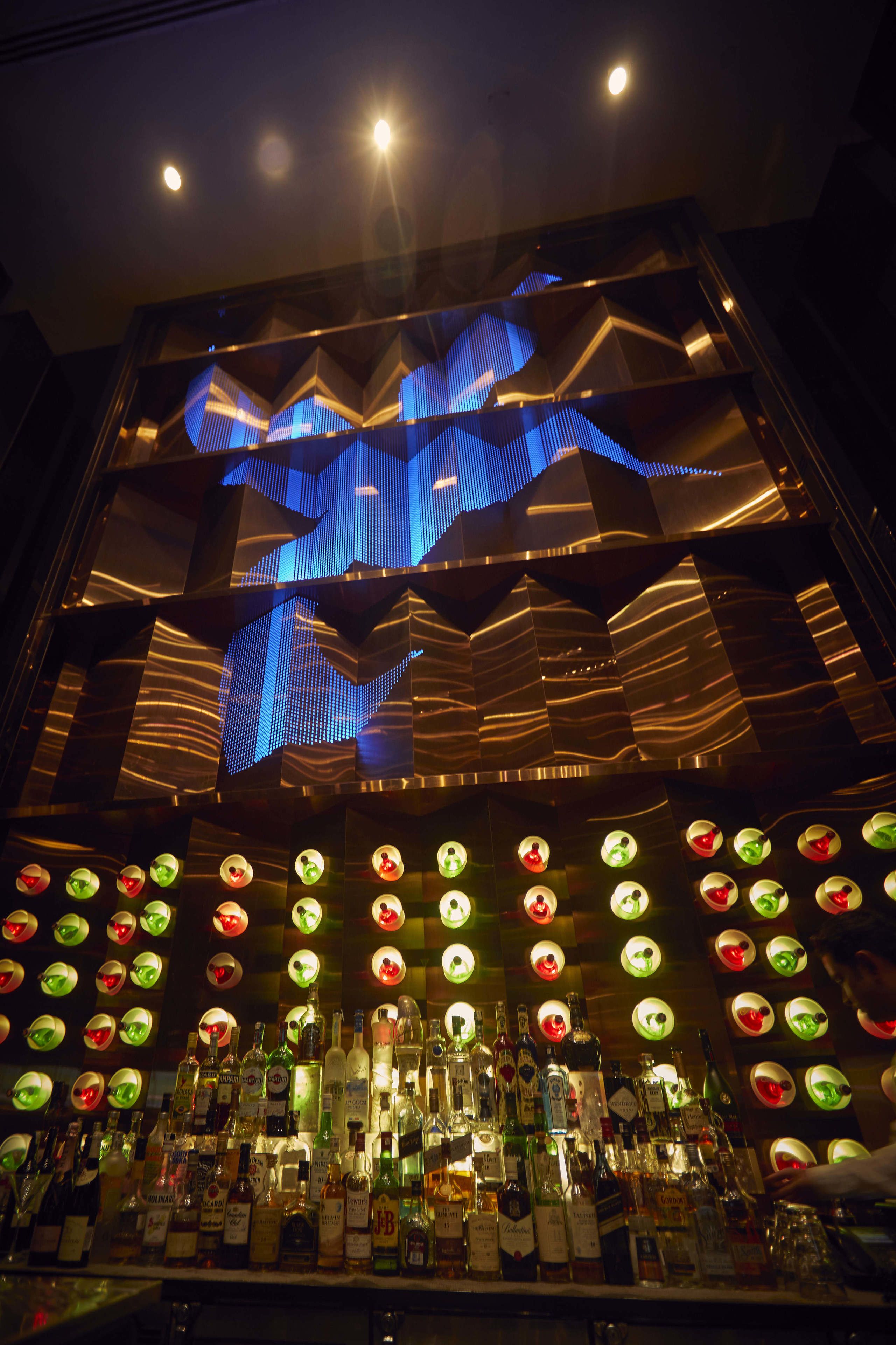 A bar area with a variety of liquor bottles and a unique ceiling design.