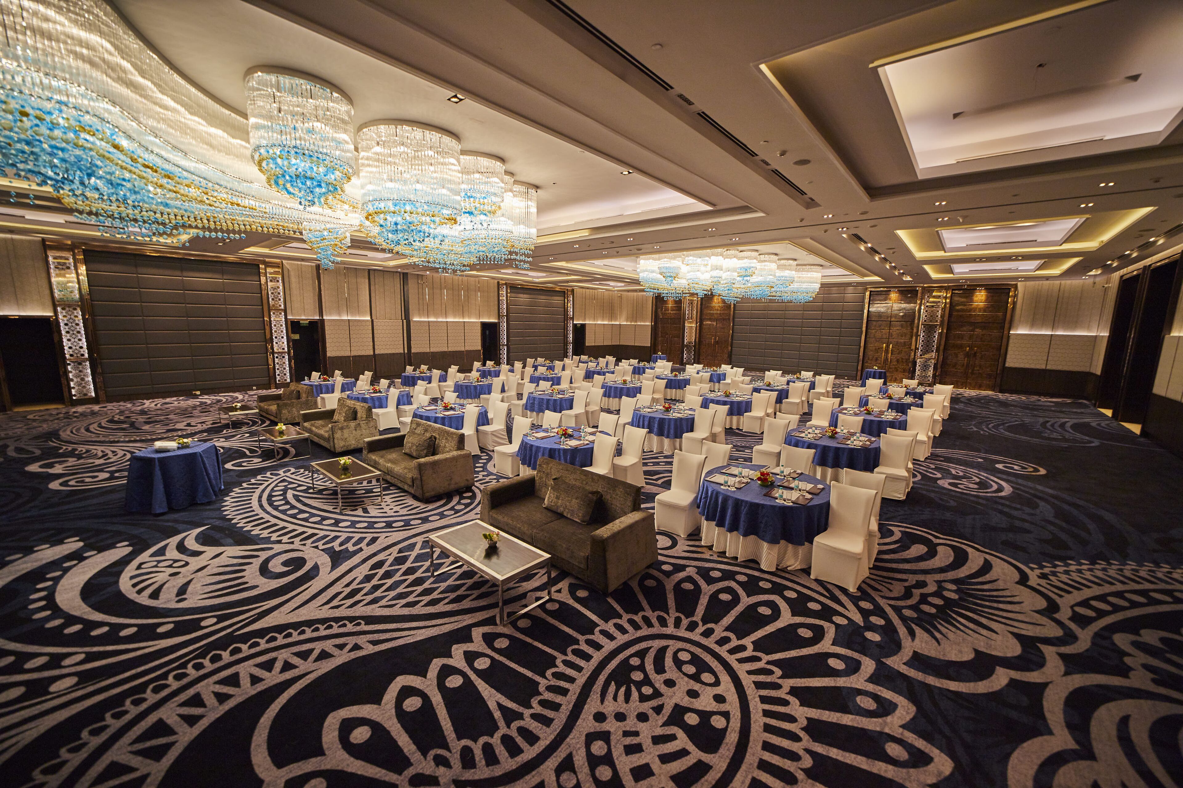 A large conference room with rows of tables and chairs, chandeliers, and a patterned carpet.
