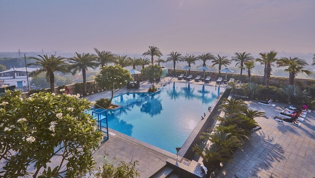 A swimming pool with sun loungers and palm trees. - Crowne Plaza New Delhi Rohini by IHG (New Delhi)