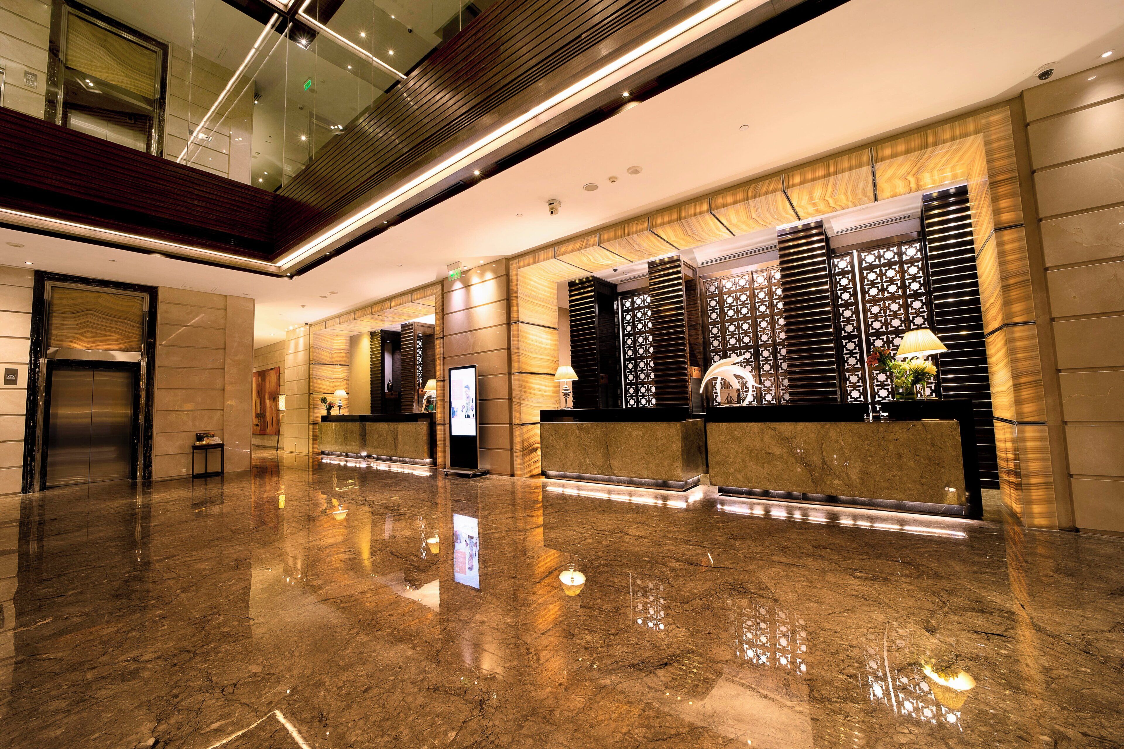 A modern lobby with a polished marble floor, a reception desk, and a glass elevator.