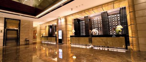A modern lobby with a polished marble floor, a reception desk, and a glass elevator.