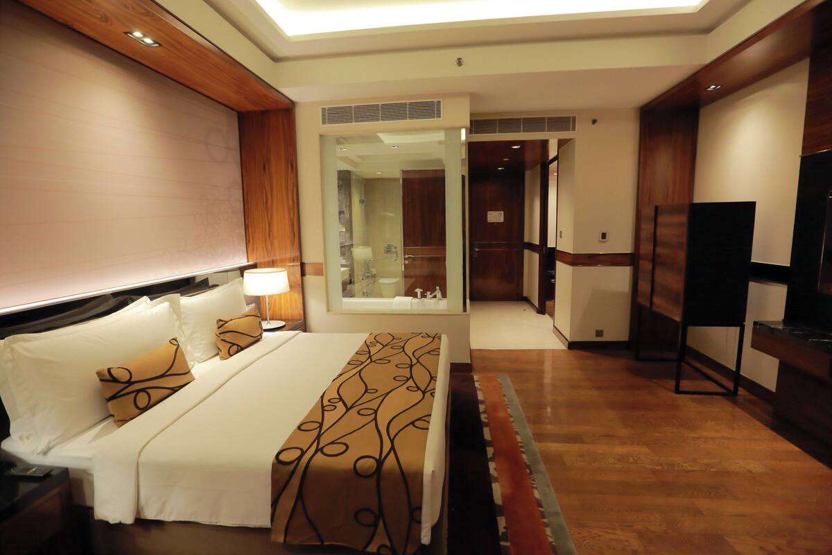 Une chambre d’hôtel équipée d’un lit, d’une télévision, d’un bureau et d’une salle de bain visible à travers une porte en verre.