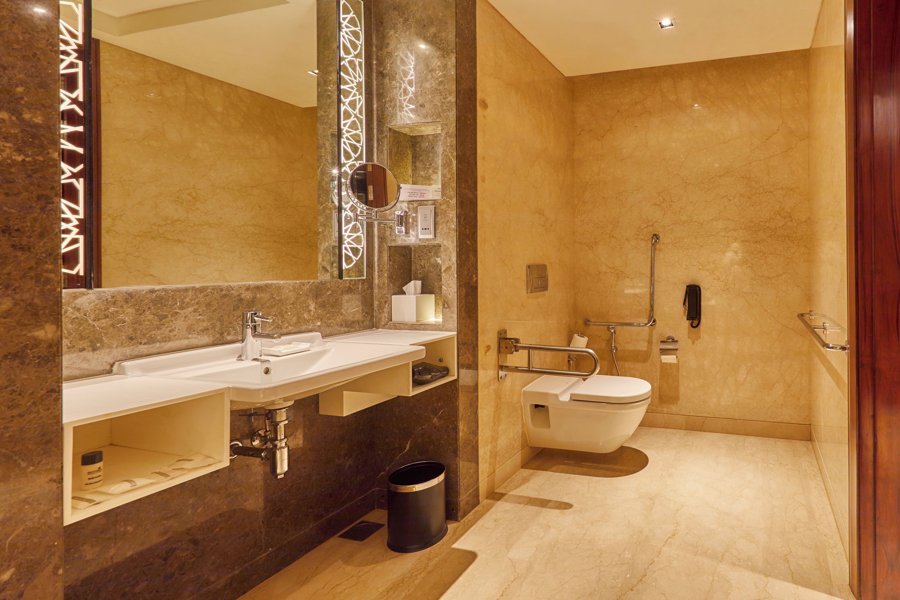 Un baño moderno con lavamanos de mármol, un espejo grande, un inodoro y una zona de ducha.