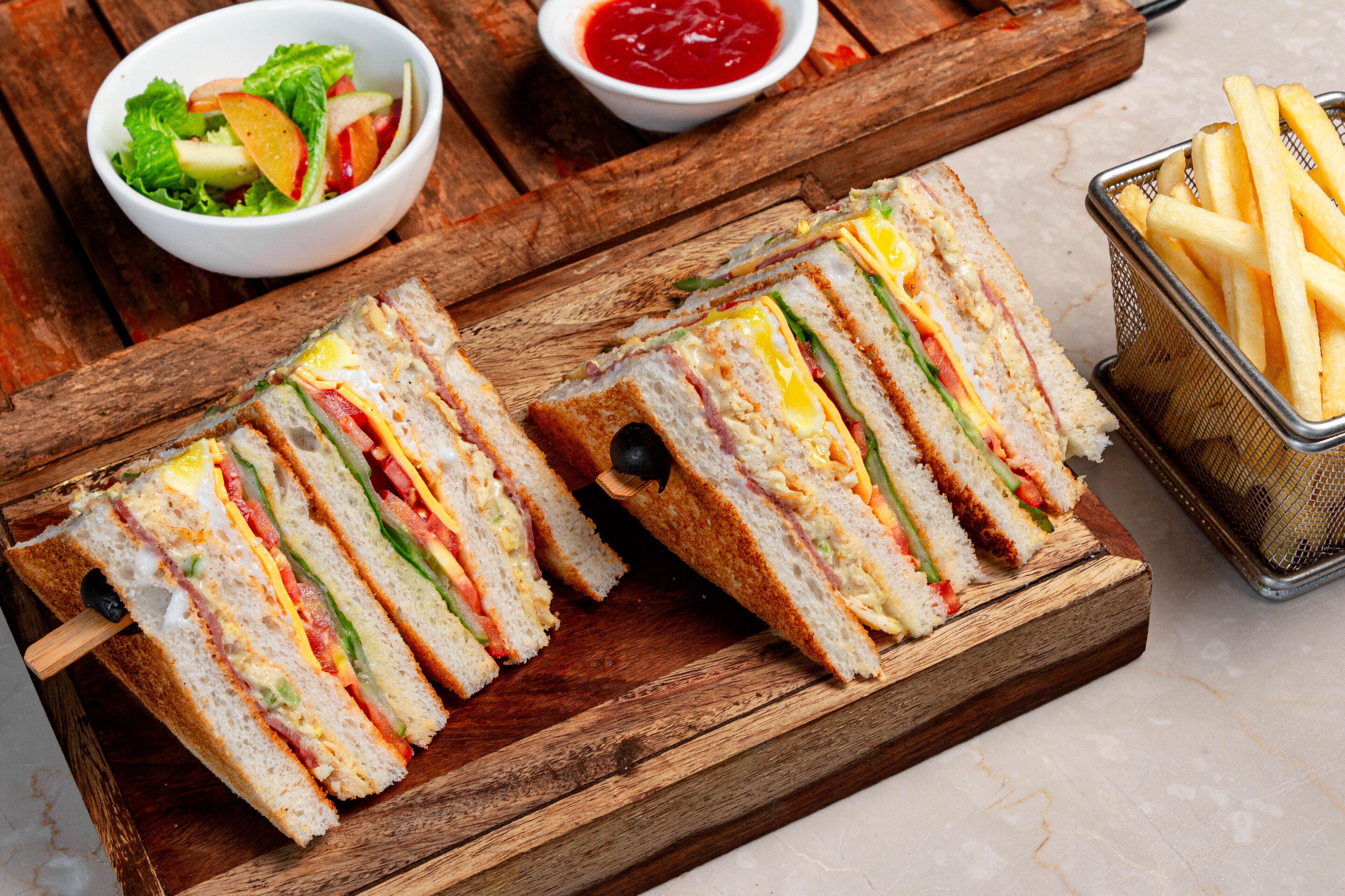 A wooden board with two sandwiches and a bowl of salad.