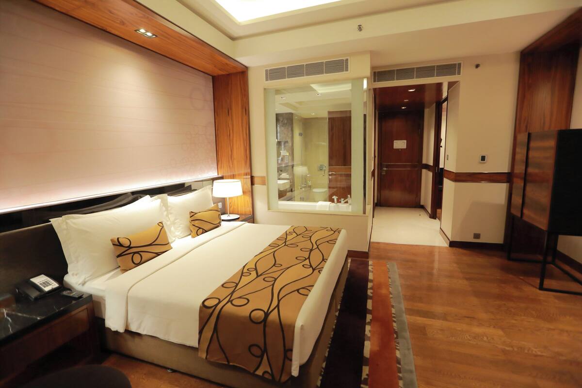 Una habitación de hotel con cama, mesita de noche, lámpara y espejo.