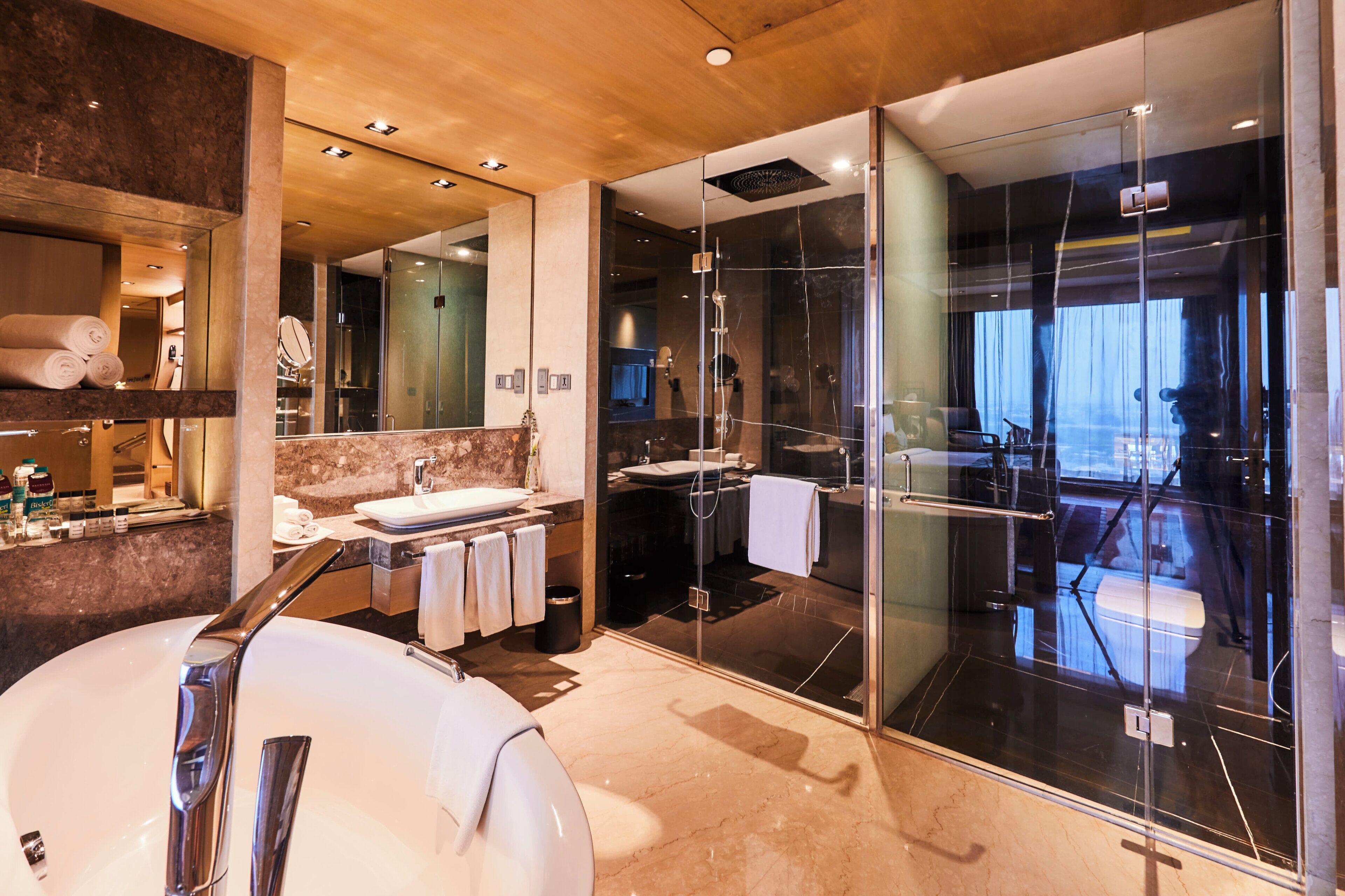 Een moderne badkamer met een groot, wit bad, een douche met glazen wand en een marmeren aanrechtblad.