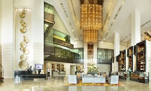 A spacious lobby with a high ceiling, modern furniture, and a central chandelier.