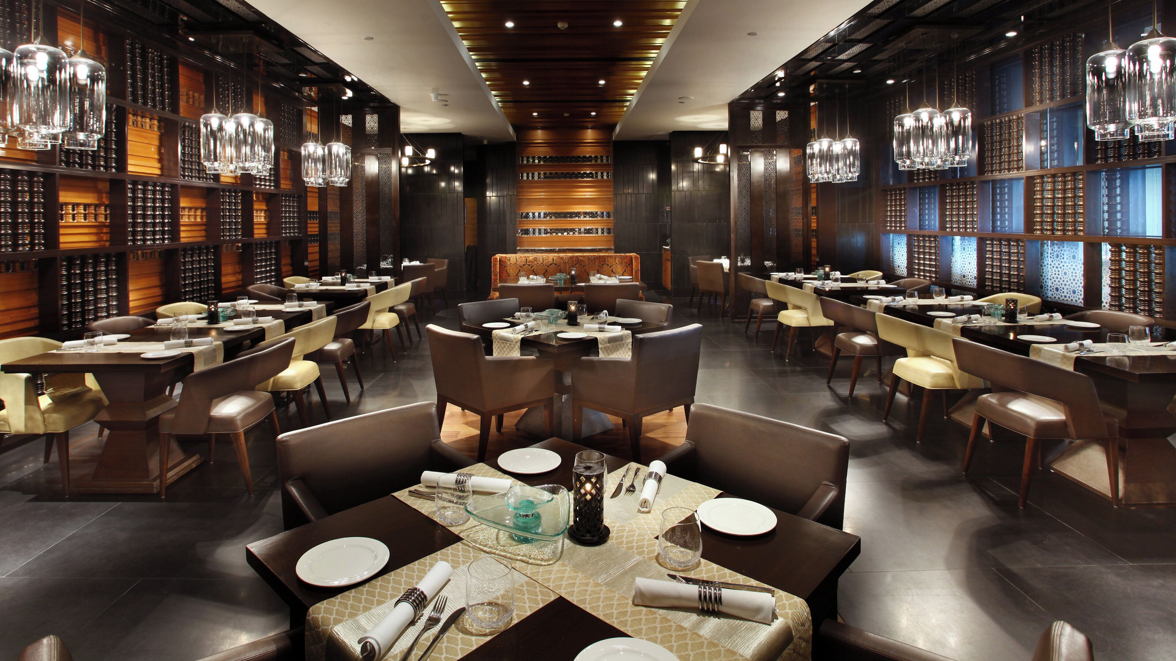 Interior de restaurante con varias mesas, sillas y lámparas colgantes.
