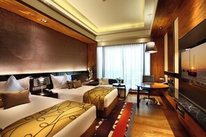 A hotel room with two beds, a desk, a TV, and a large window with curtains.