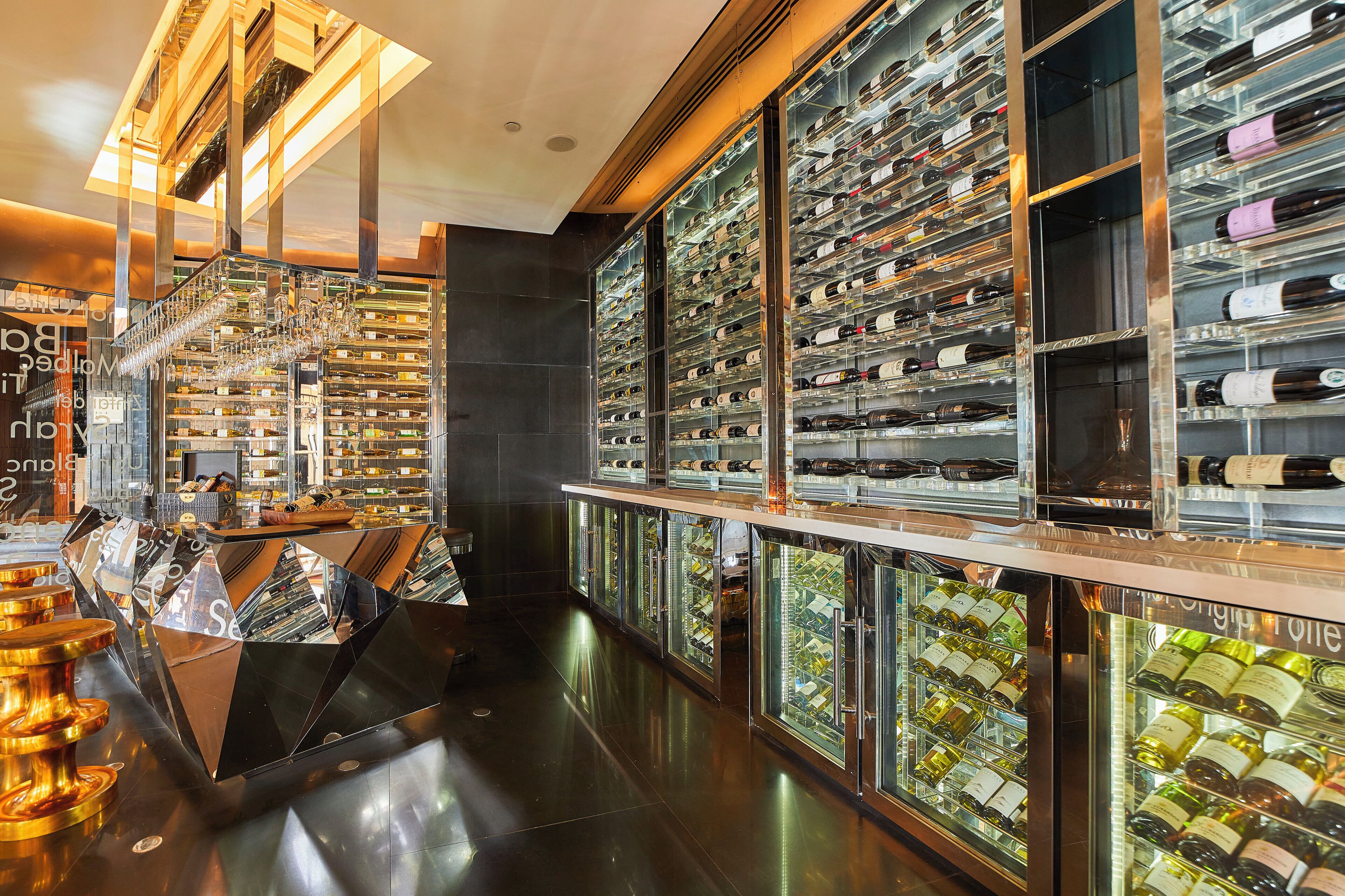 A wine cellar with multiple rows of wine bottles, a glass display case, and a polished floor.
