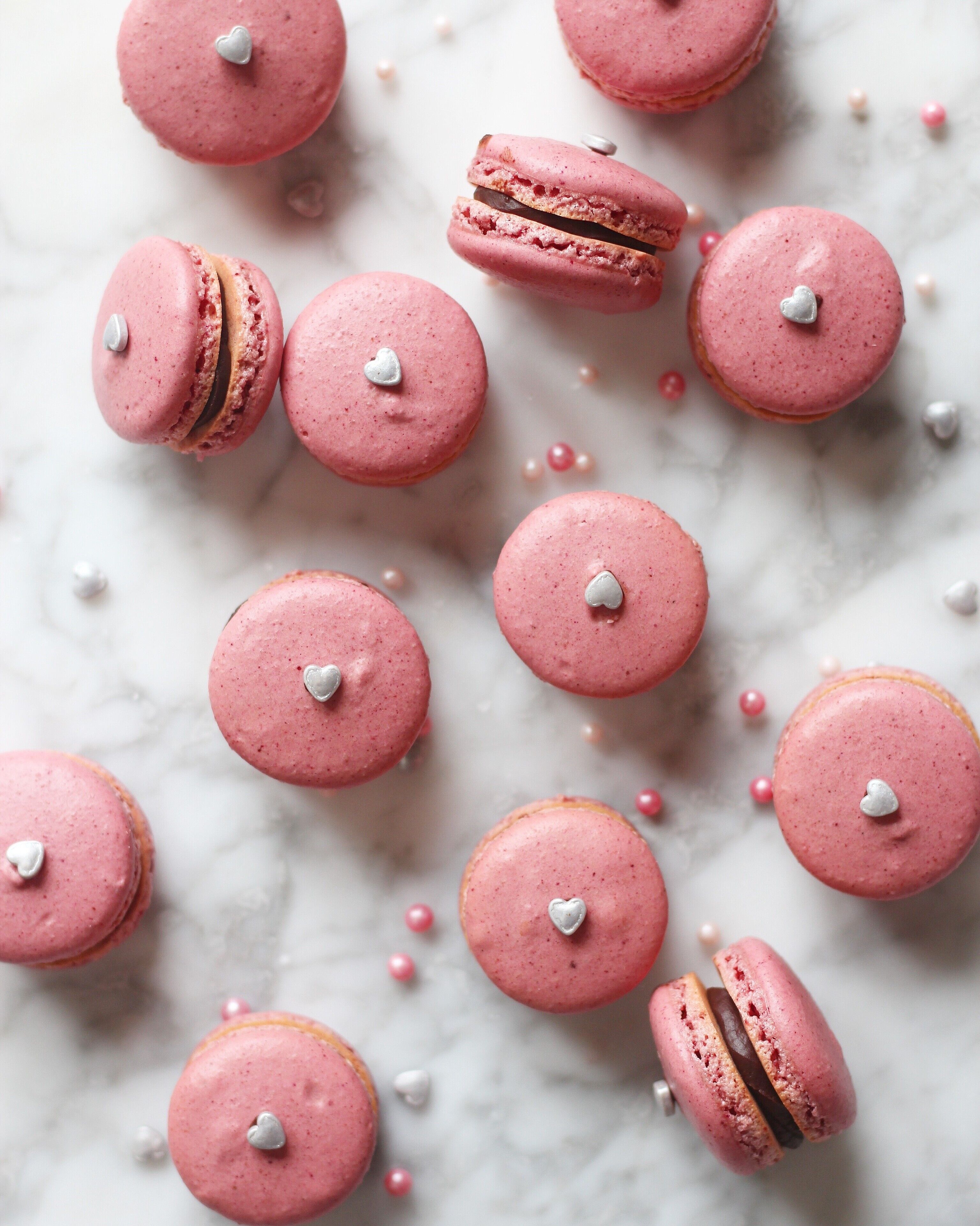 Des macarons roses ornés de cœurs blancs, posés sur une surface en marbre.