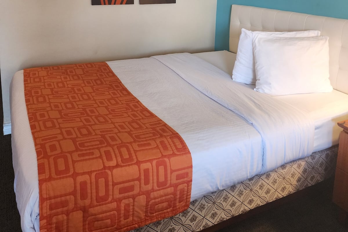 Habitación de hotel con cama, una manta estampada, cabecero y dos cuadros abstractos en la pared.