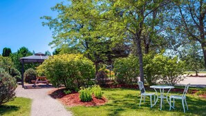 Un giardino con un vialetto ghiaioso, tavoli da picnic e sedie in metallo bianco.