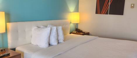 Habitación de hotel con una cama grande, dos lámparas de noche, una mesita de noche y una obra de arte colgada en la pared.