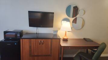 A hotel room with a desk, a television, a lamp, a chair, and a cabinet.