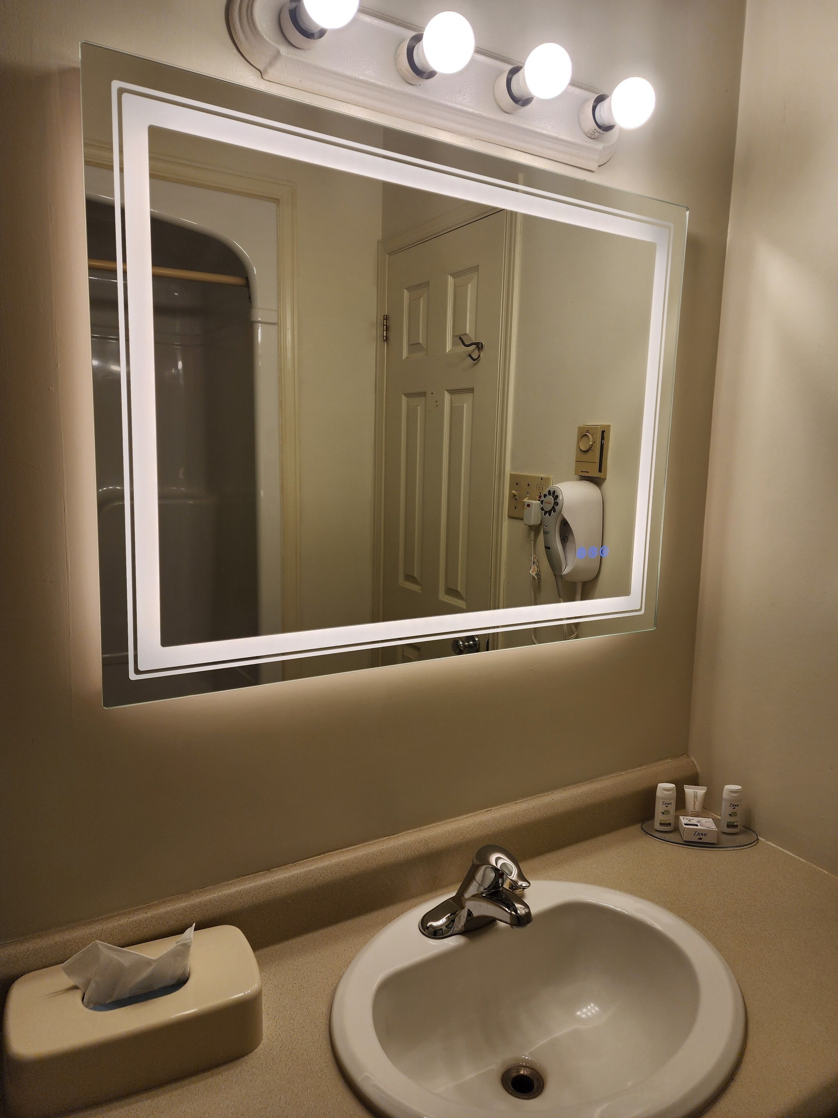 A bathroom with a large mirror, a sink, and a towel dispenser.