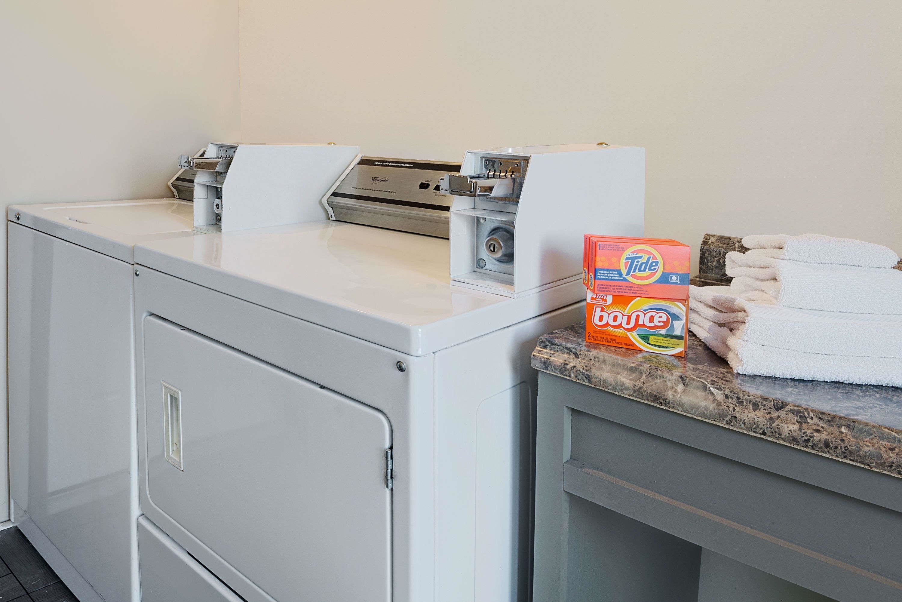 A laundry area with a washing machine, a dryer, and a box of Tide Bounce detergent on a countertop.
