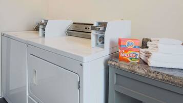 A laundry area with a washing machine, a dryer, and a box of Tide Bounce detergent on a countertop.