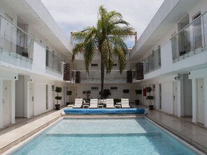 A modern indoor pool with a central palm tree, surrounded by white walls and multiple balconies.
