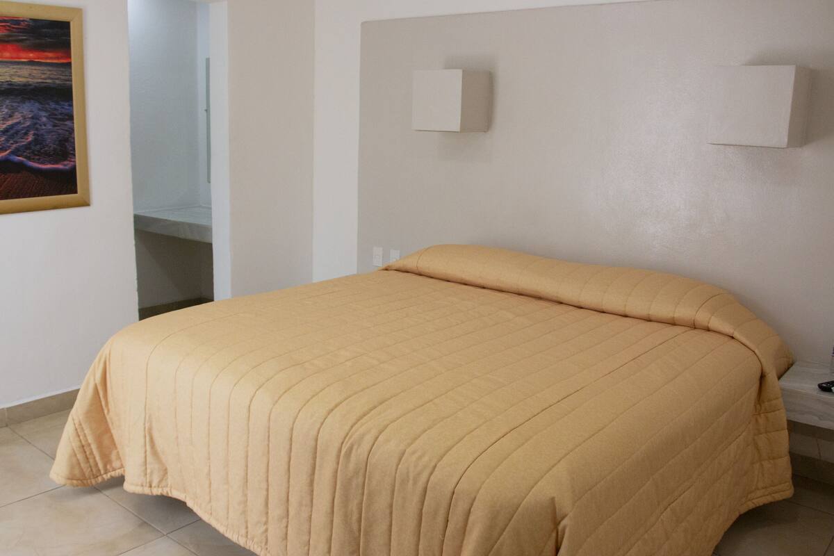 A bedroom with a large bed, a nightstand, a wall-mounted light, and a painting on the wall.