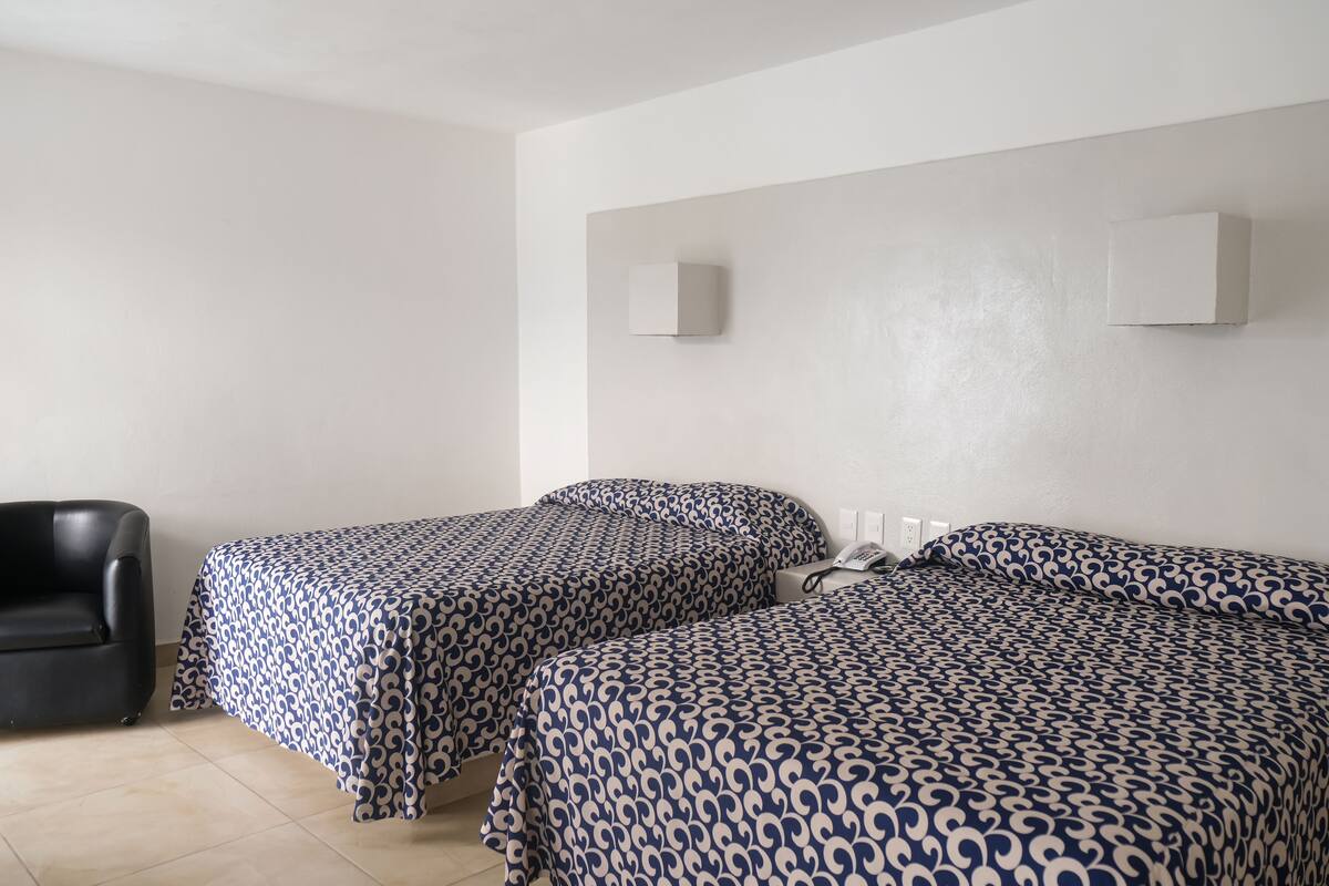 A hotel room with two single beds, a black chair, and two wall-mounted light fixtures.