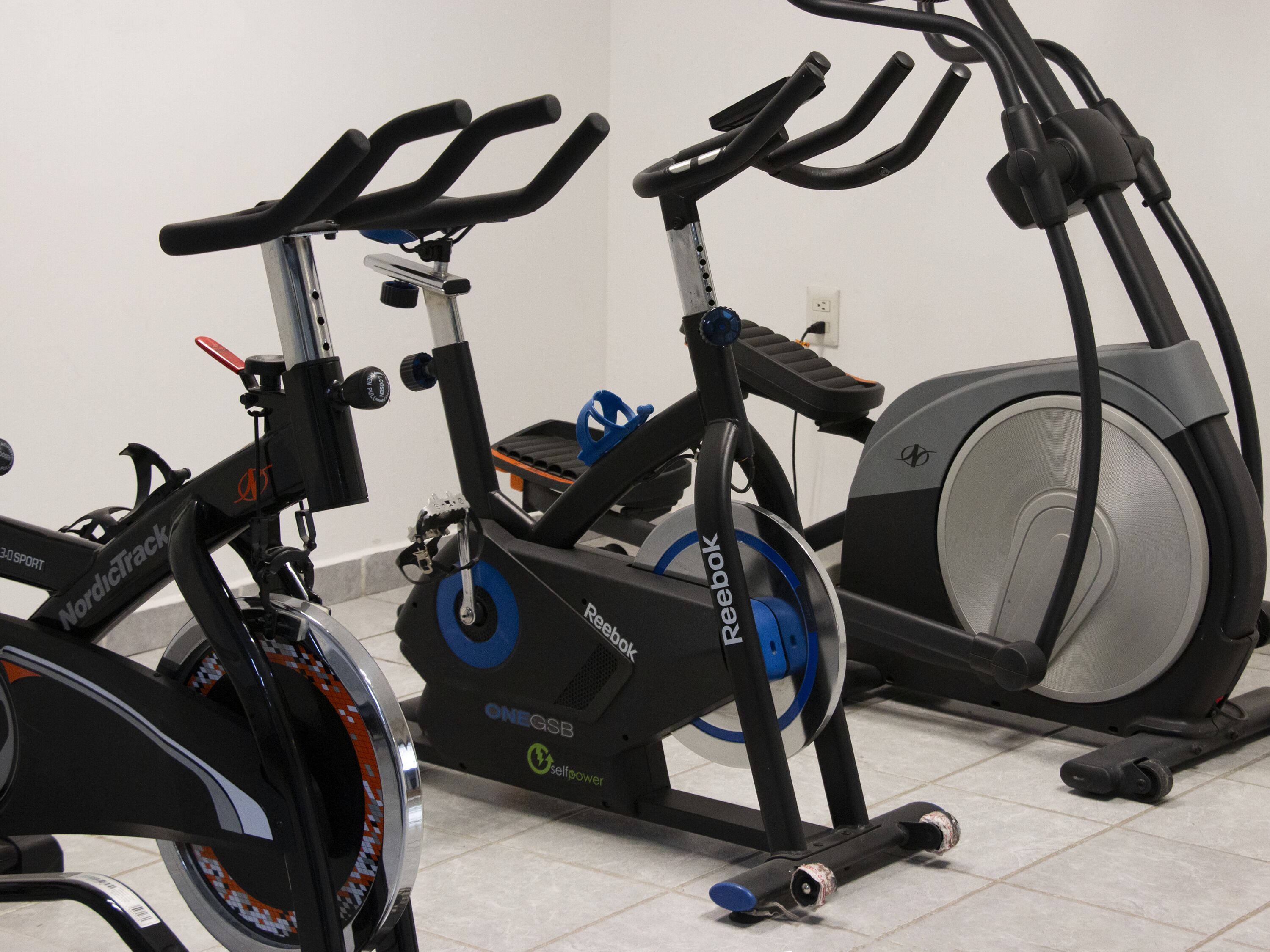 A stationary bike and a treadmill in a room with white walls and tiled flooring.