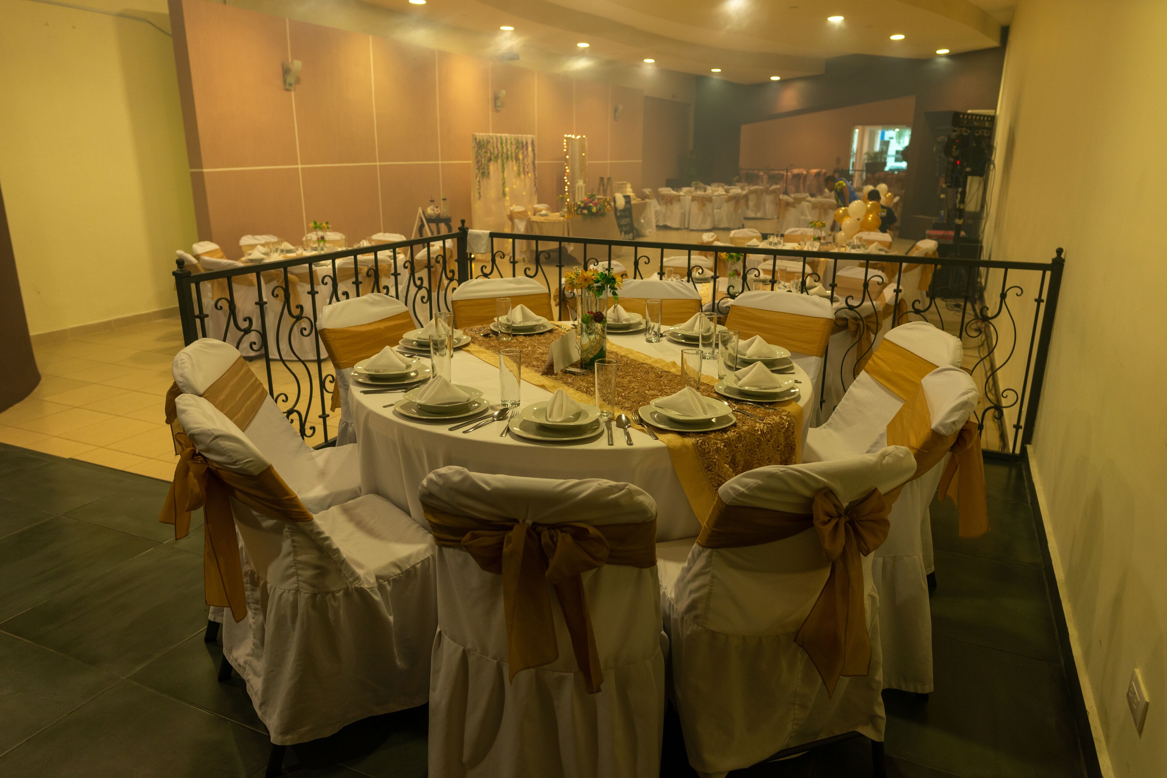 A banquet hall with round tables set for a formal event, featuring white tablecloths, gold sashes, and neatly arranged tableware.