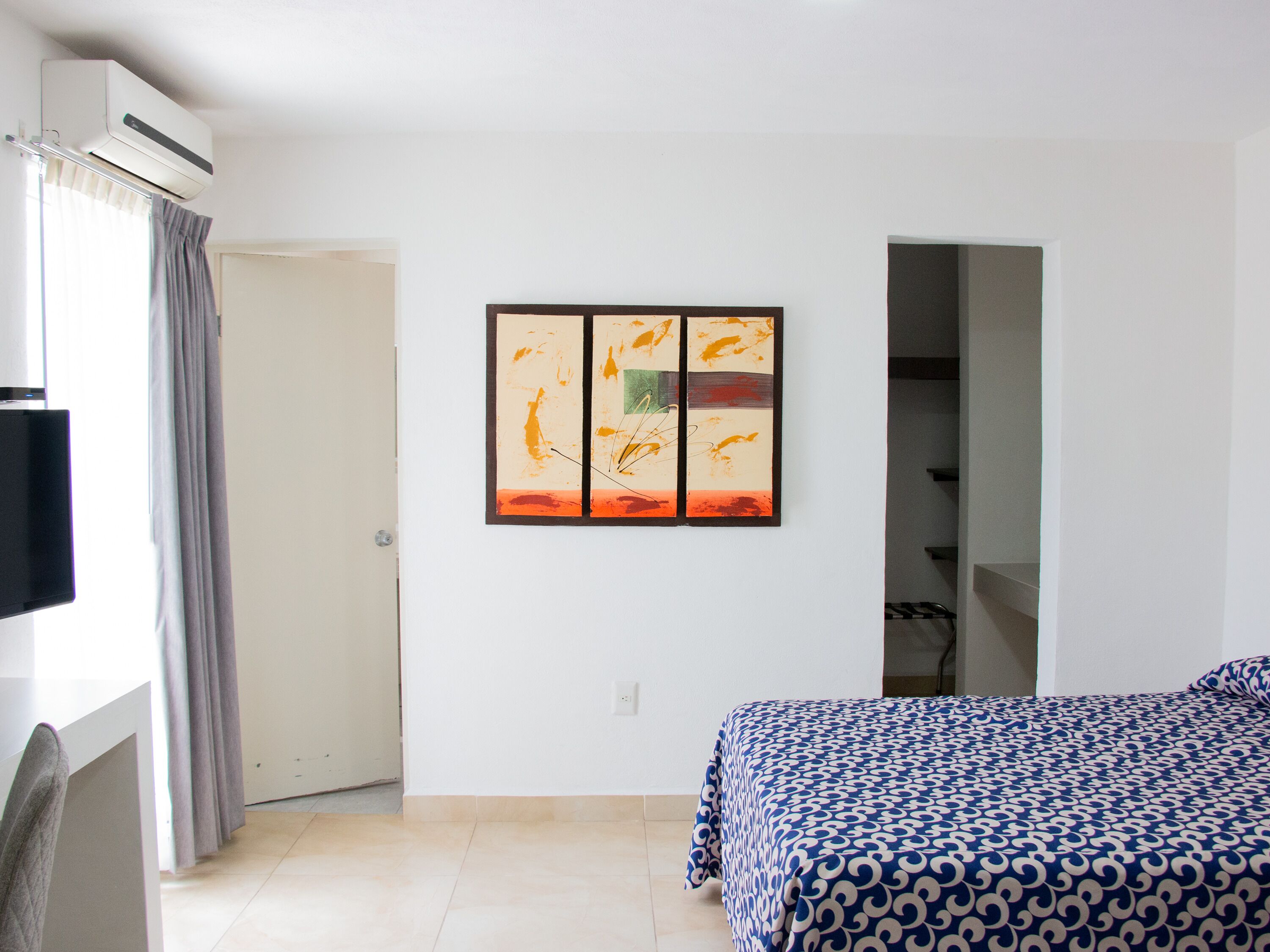 Quarto de hotel com cama, televisão de tela plana, ar condicionado e um quadro na parede.