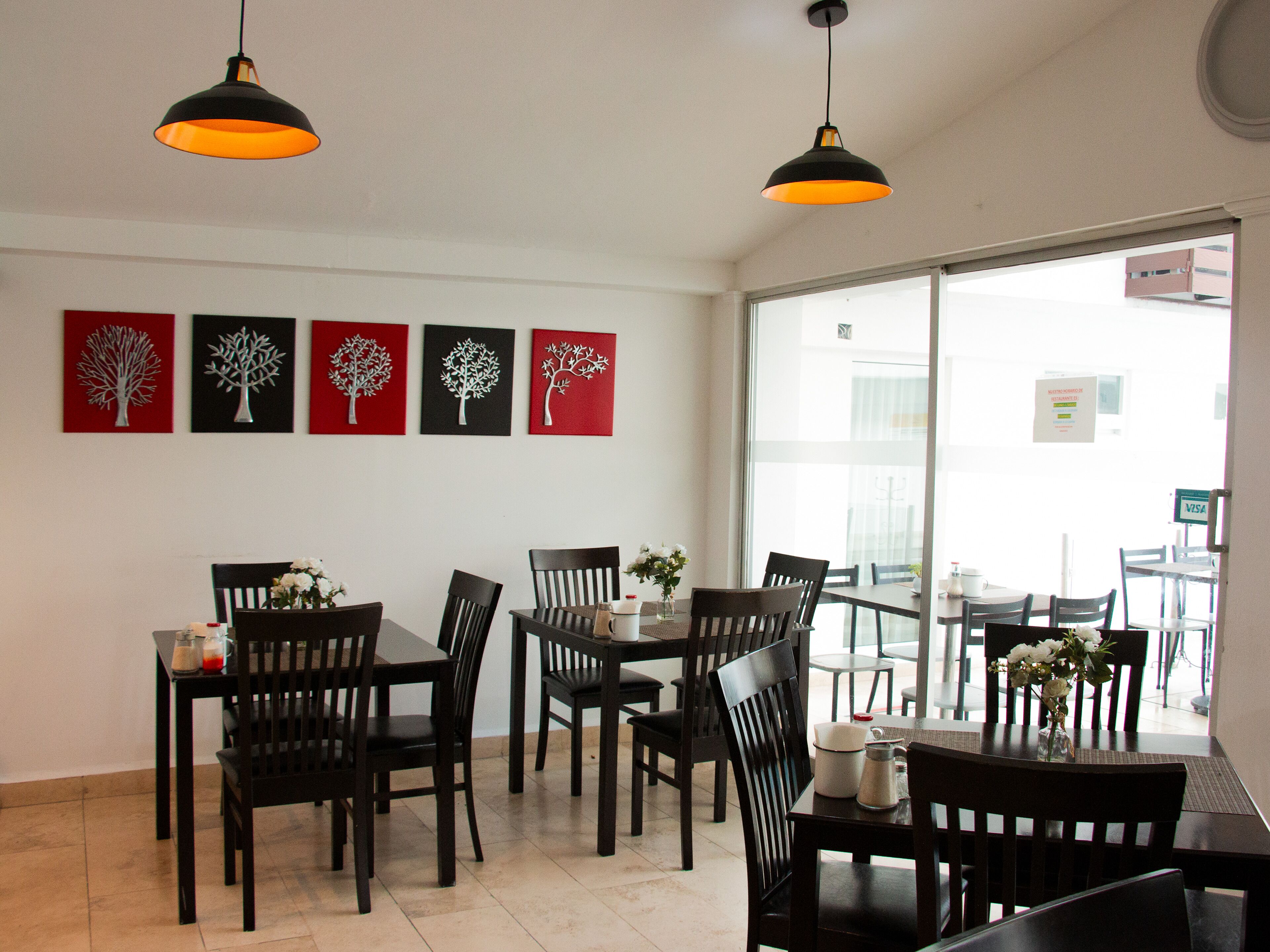 A dining area with wooden tables and chairs, a large window with a view of buildings, and artwork on the wall.