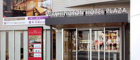 Exterior del Hotel Washington Plaza con un cartel grande, entrada de vidrio y suelo de baldosas.