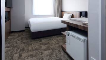 A hotel room with a bed, a desk, a small refrigerator, and a television on the wall.