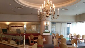 A hotel lobby with a grand chandelier, a reception desk, and a seating area with round tables and chairs.